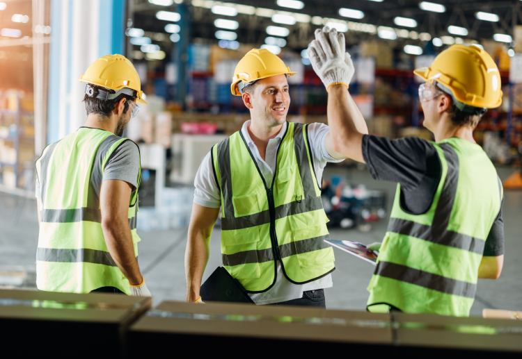 Industrial workers in hi-vis vests, safety gloves and hard hats high-five on the manufacturing floor